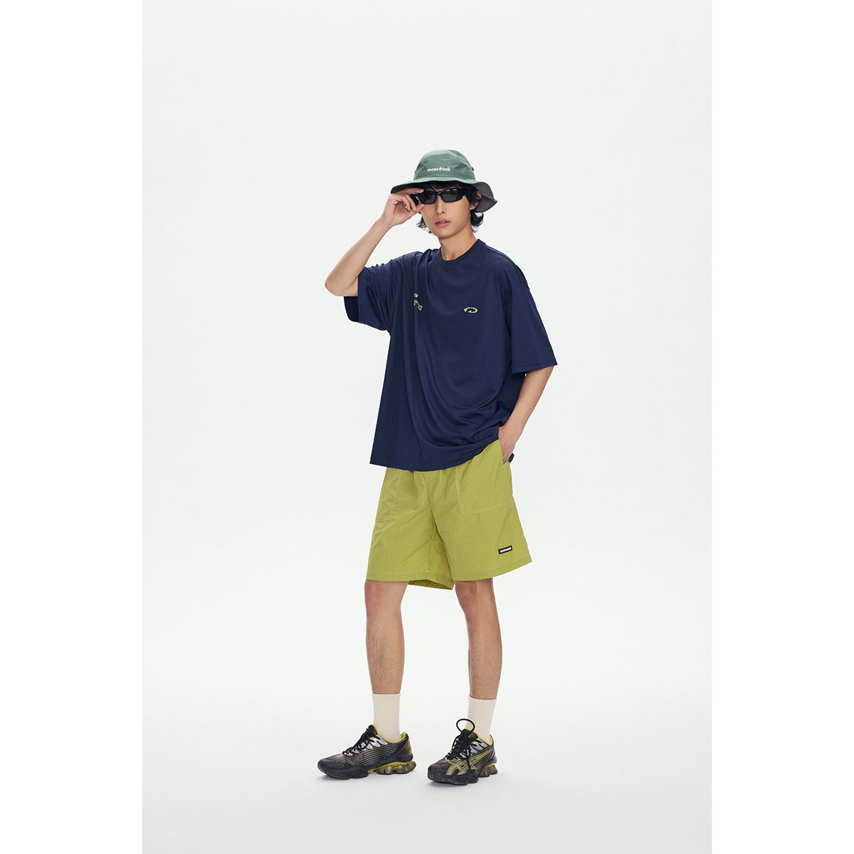 Model wearing an oversized navy T-shirt with small lime graphics and lime shorts, styled with a green bucket hat.