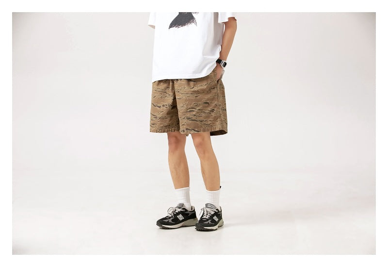 Front view of a person wearing loose brown camouflage-print shorts and a white T-shirt.