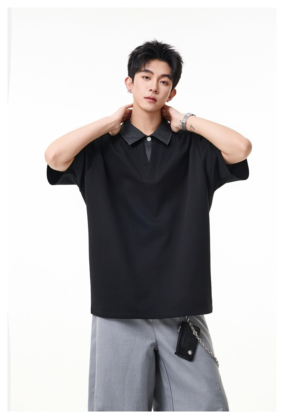 Model wearing an oversized black polo-style shirt with a charcoal collar and light gray trousers.