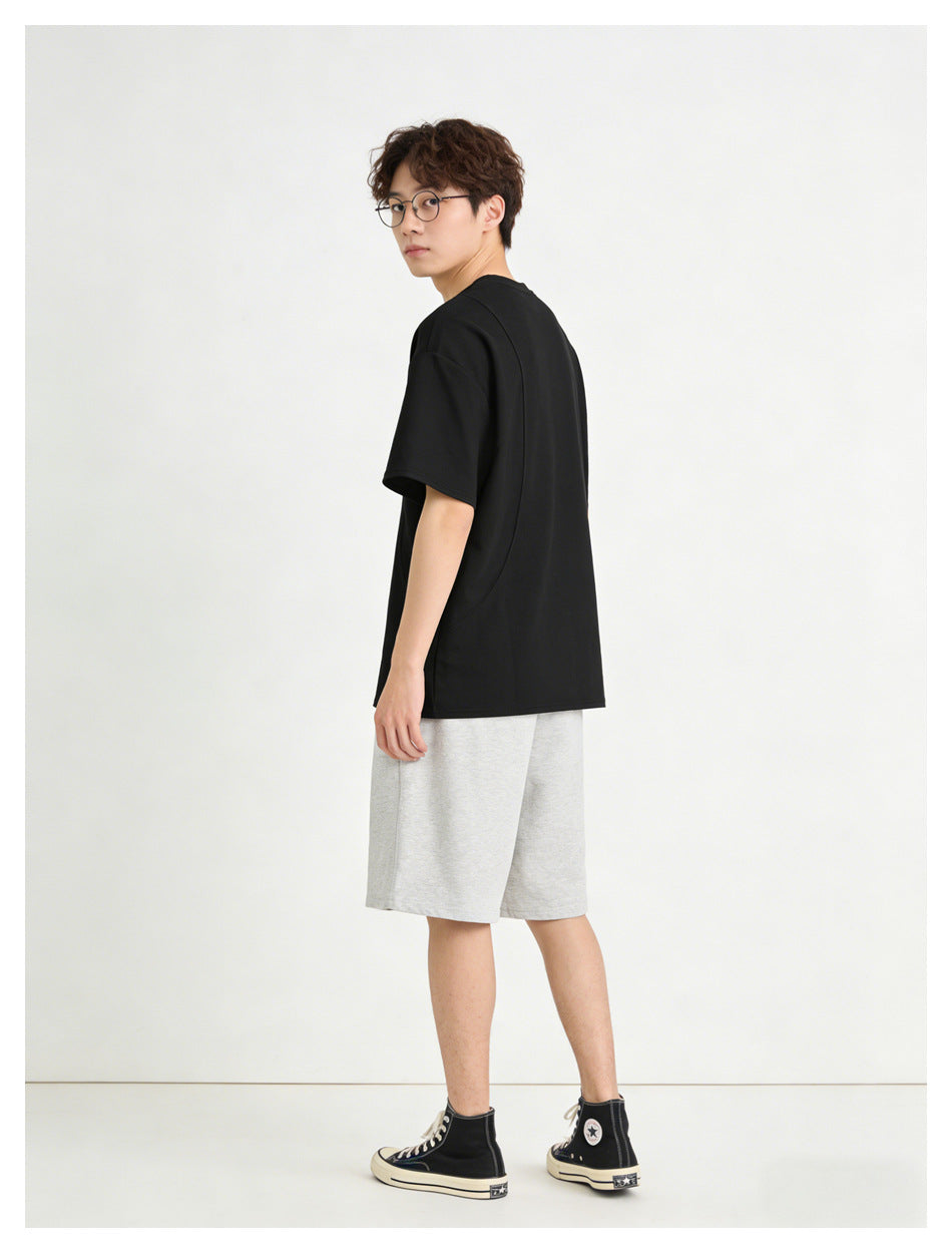 Model in a loose black short-sleeve T-shirt and light gray knee-length shorts, seen from a turned rear angle.