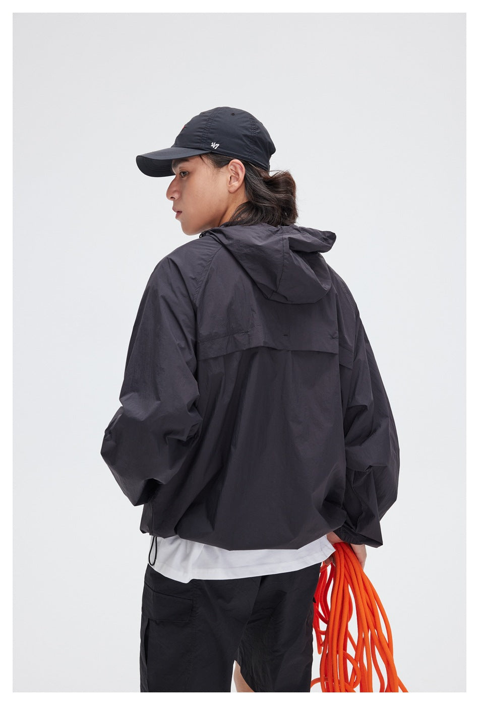 Back view of a model wearing a black hooded jacket with a rear yoke and hem drawcord.