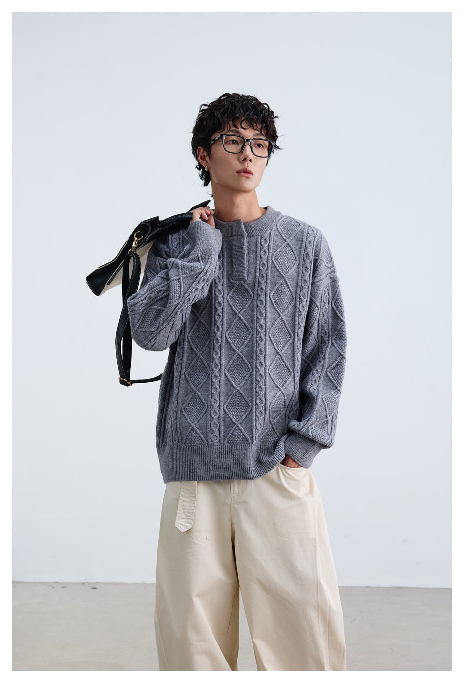 Model wearing a gray cable-knit sweater with cream wide-leg pants, holding a black and white bag over the shoulder