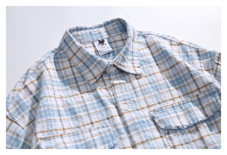 Close-up of a pale blue and tan plaid shirt showing its collar, buttons, chest pocket, and frayed trim.