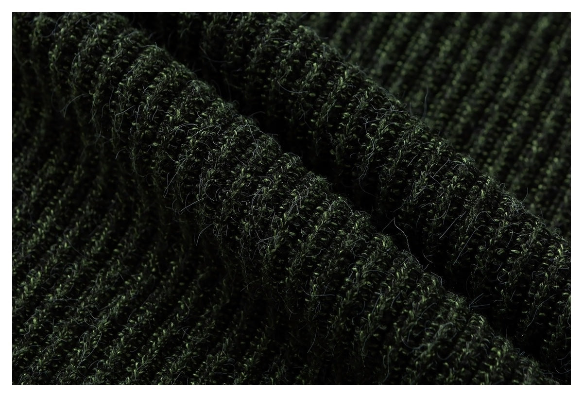 Macro view of dark green knitted fabric with a thick, raised rib and visible loose fibers.