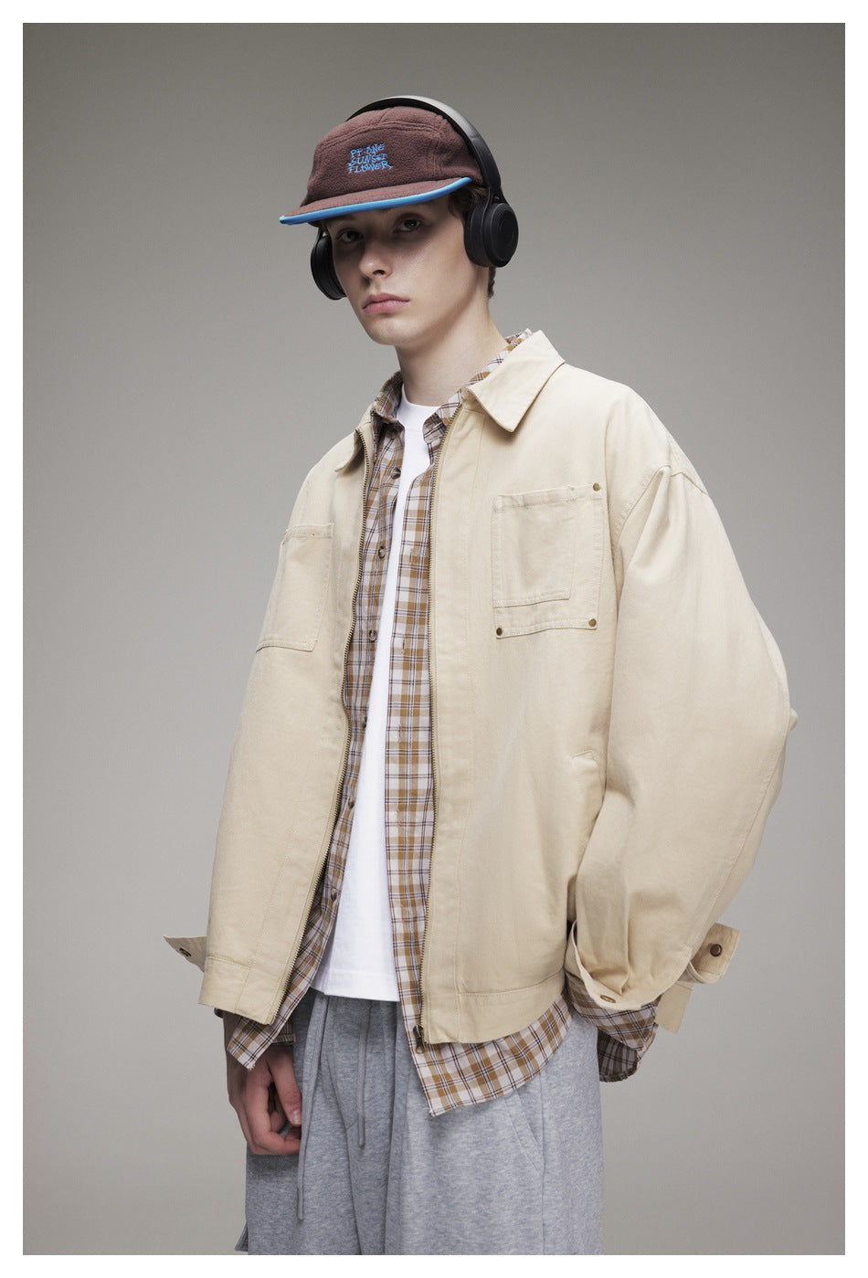 Model wearing a cream zip-front jacket with chest pockets over a plaid shirt and white tee.