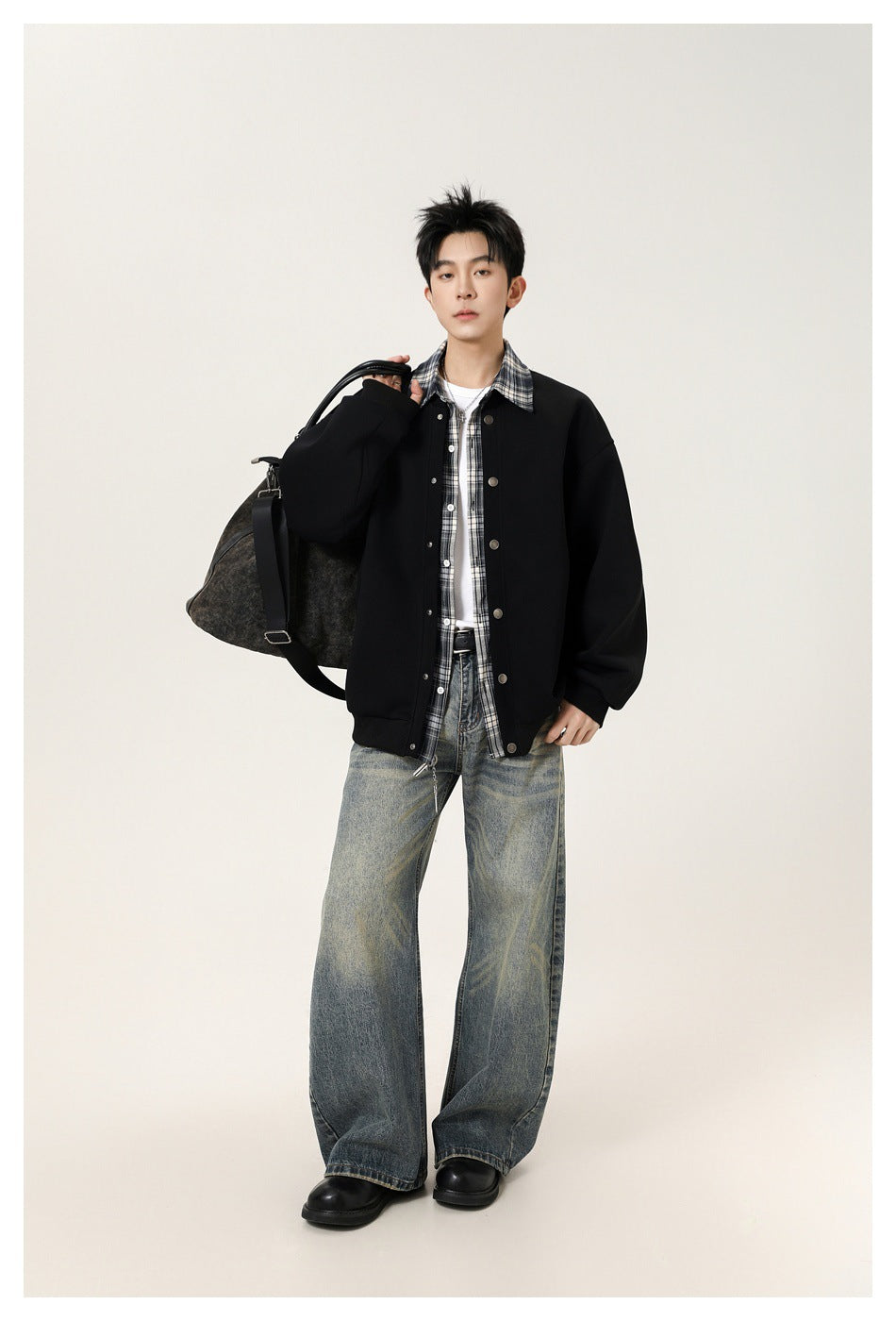 Model wearing a black snap-front jacket with a plaid collar, layered over a checked shirt and white tee.