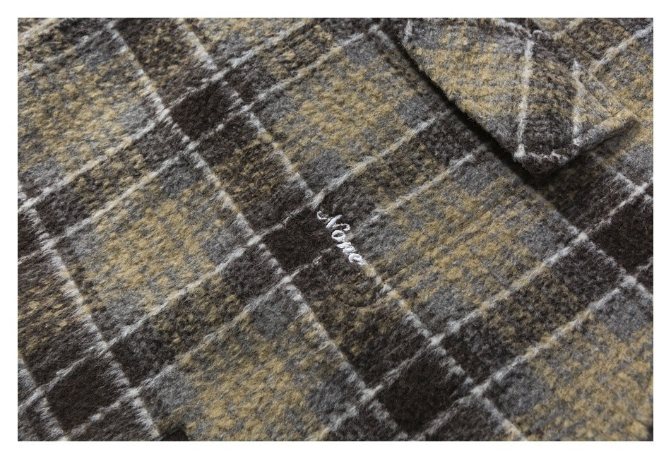Close-up of brown, charcoal and tan plaid fabric with a small white embroidered mark.