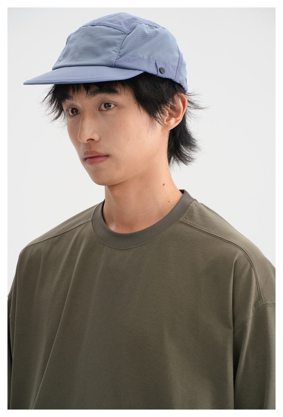 Close-up of a man in an olive crew-neck long-sleeve shirt and a light blue paneled cap.