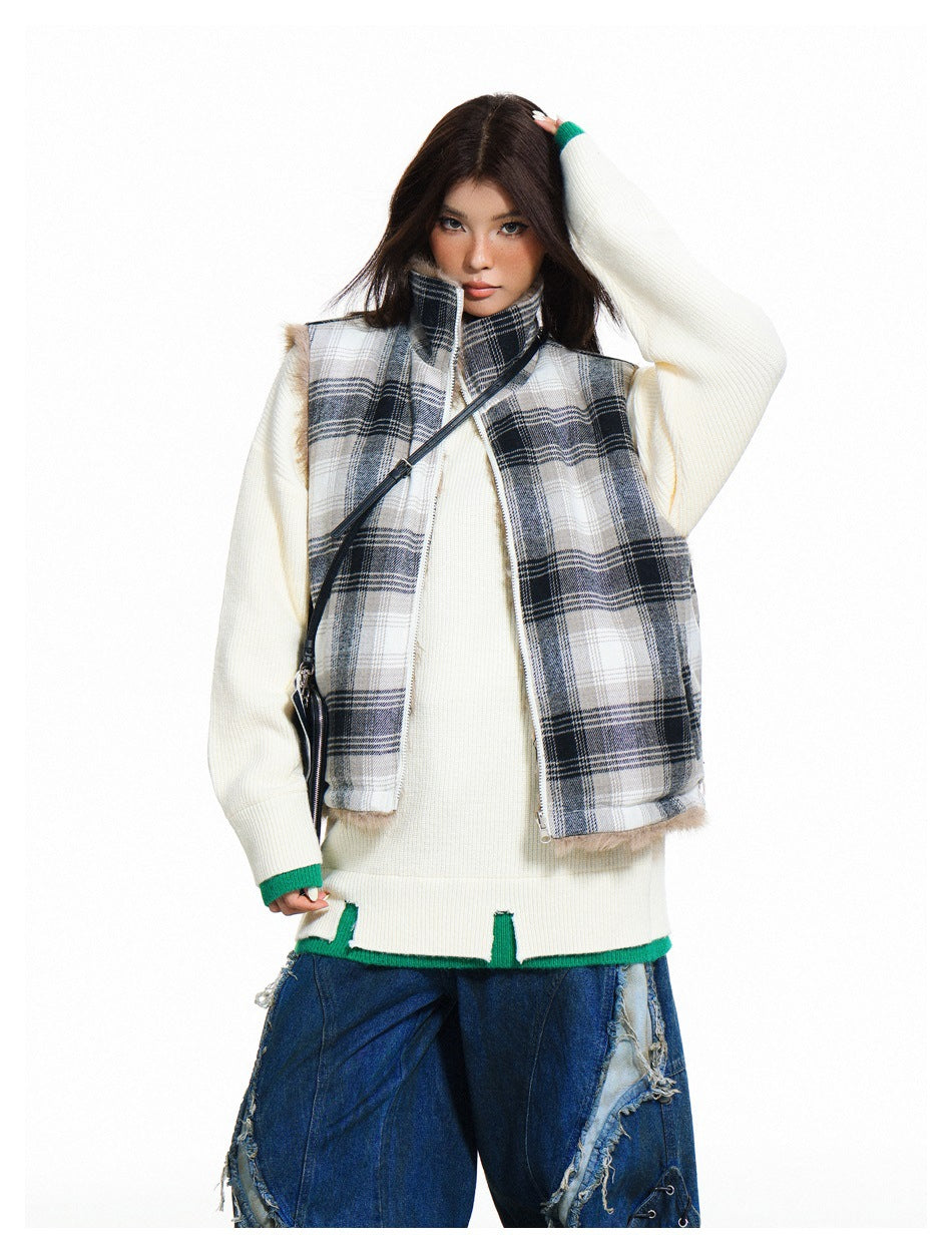 Model wearing an open gray plaid vest with a stand collar and fur trim over a cream sweater and blue jeans.