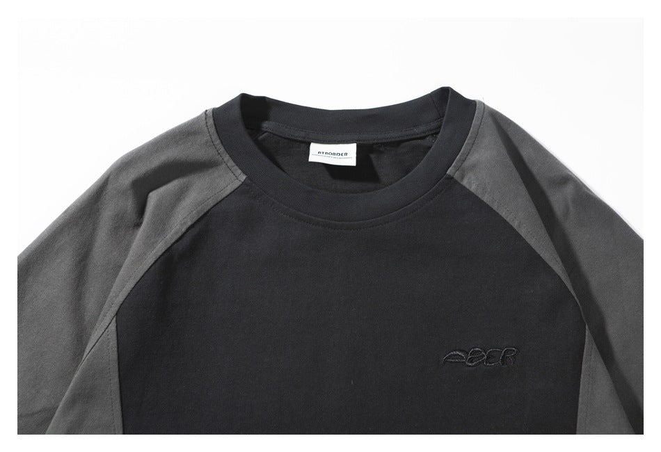 Close-up of a black raglan shirt's charcoal shoulder panels, crew neck, inner label, and small chest embroidery.