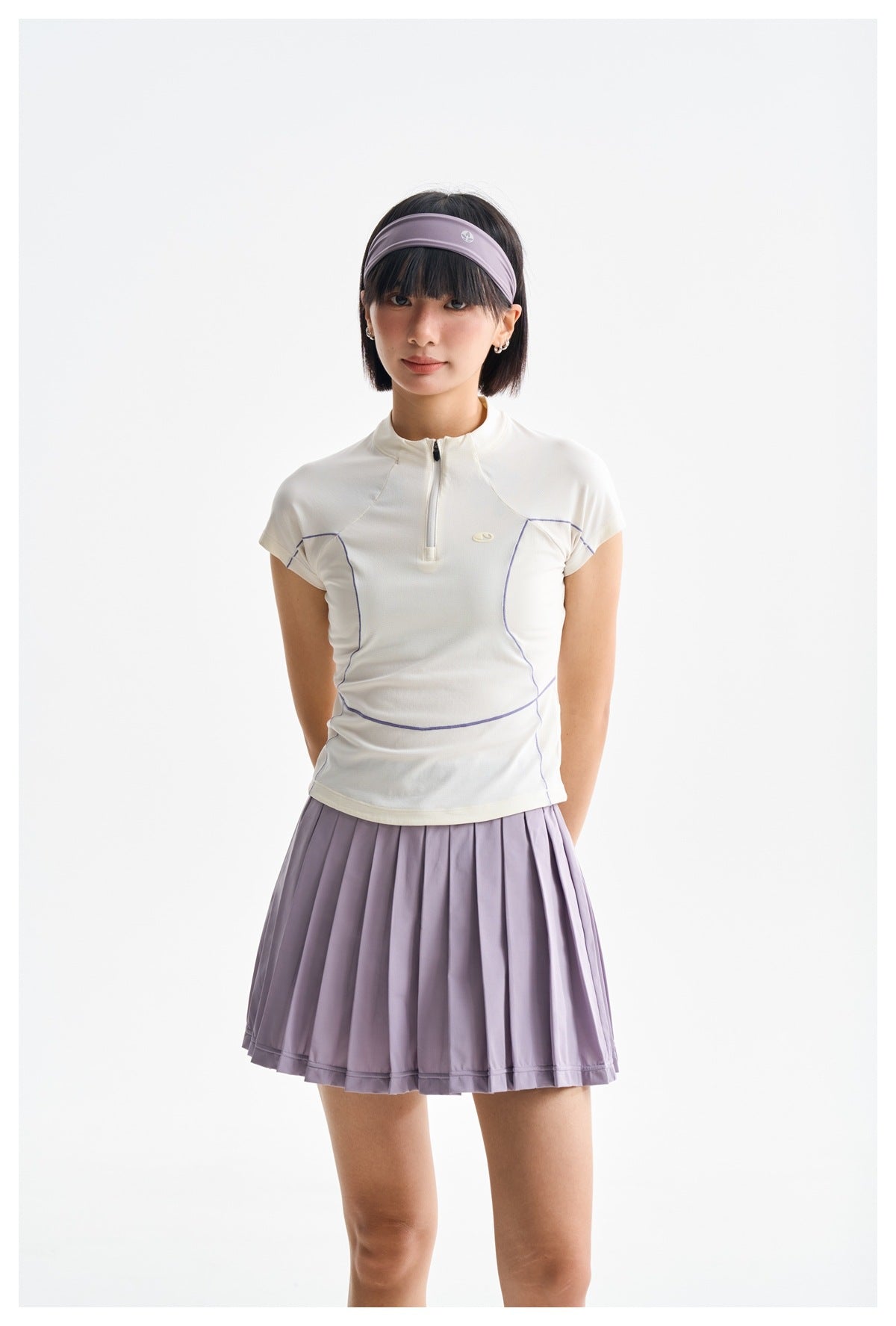 Front view of a model in a white quarter-zip top with lilac piping and a pleated lilac skirt.