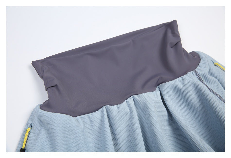 Close-up of light blue textured garment fabric joined to a wide charcoal-gray panel, with yellow zipper pulls at the sides.