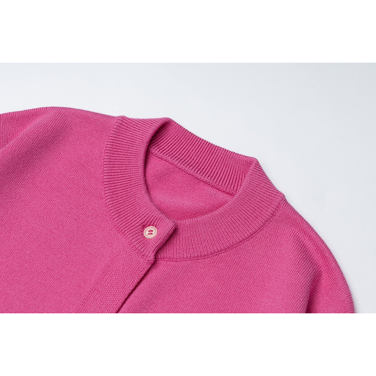 Close-up of a bright pink cardigan's ribbed crew neck and button placket.
