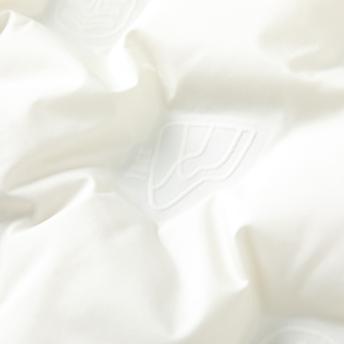 Close-up of an ivory jacket showing a subtle raised emblem on the fabric.