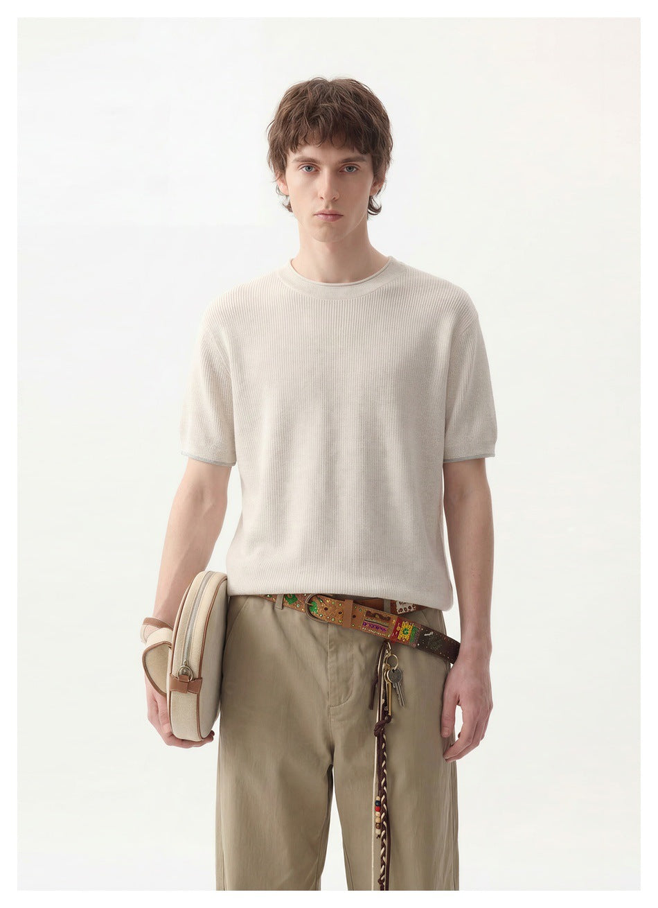 Model wearing an ivory short-sleeve knit crewneck with taupe trousers, shown from the front.