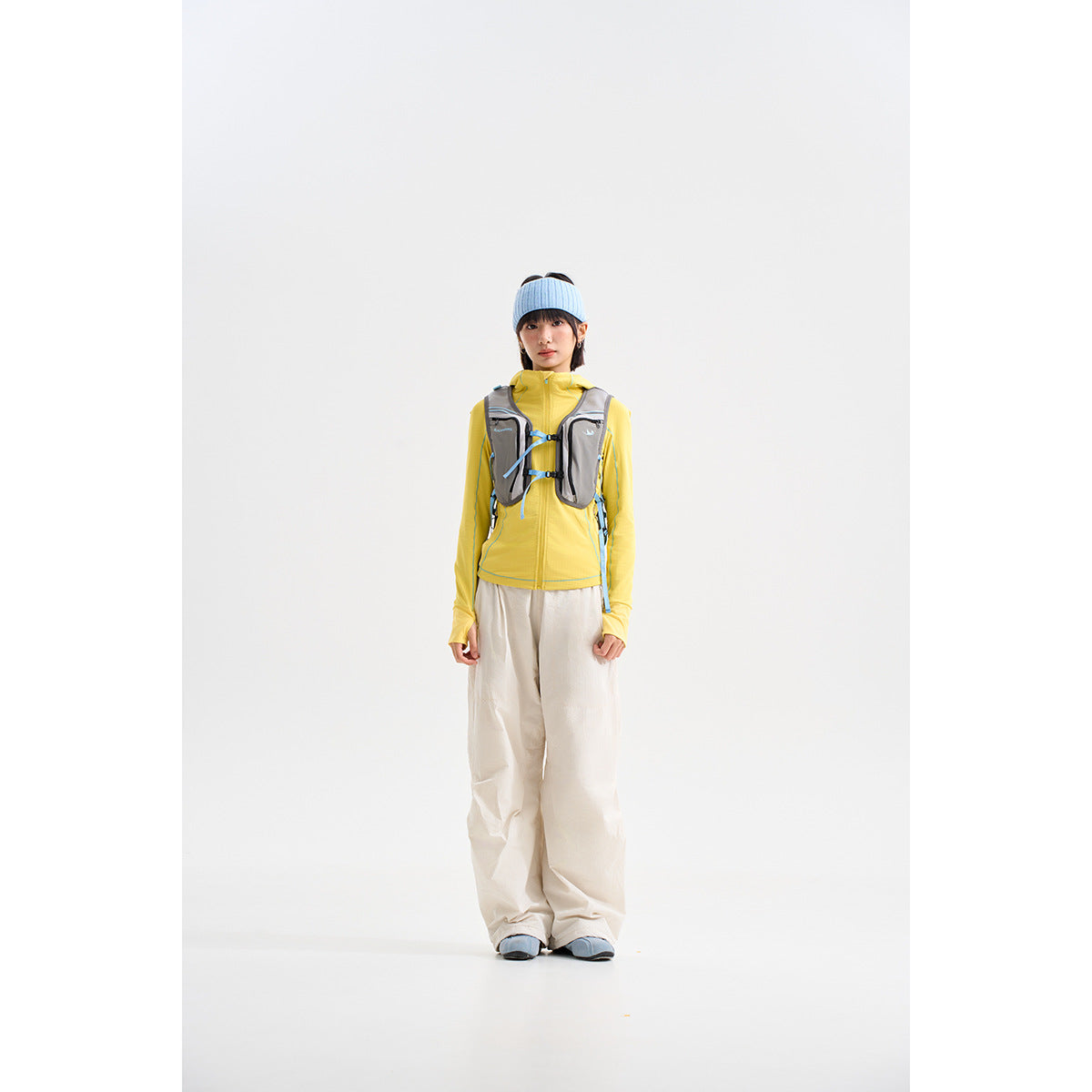 Model wearing a yellow long-sleeve top, gray utility vest, and loose cream pants.