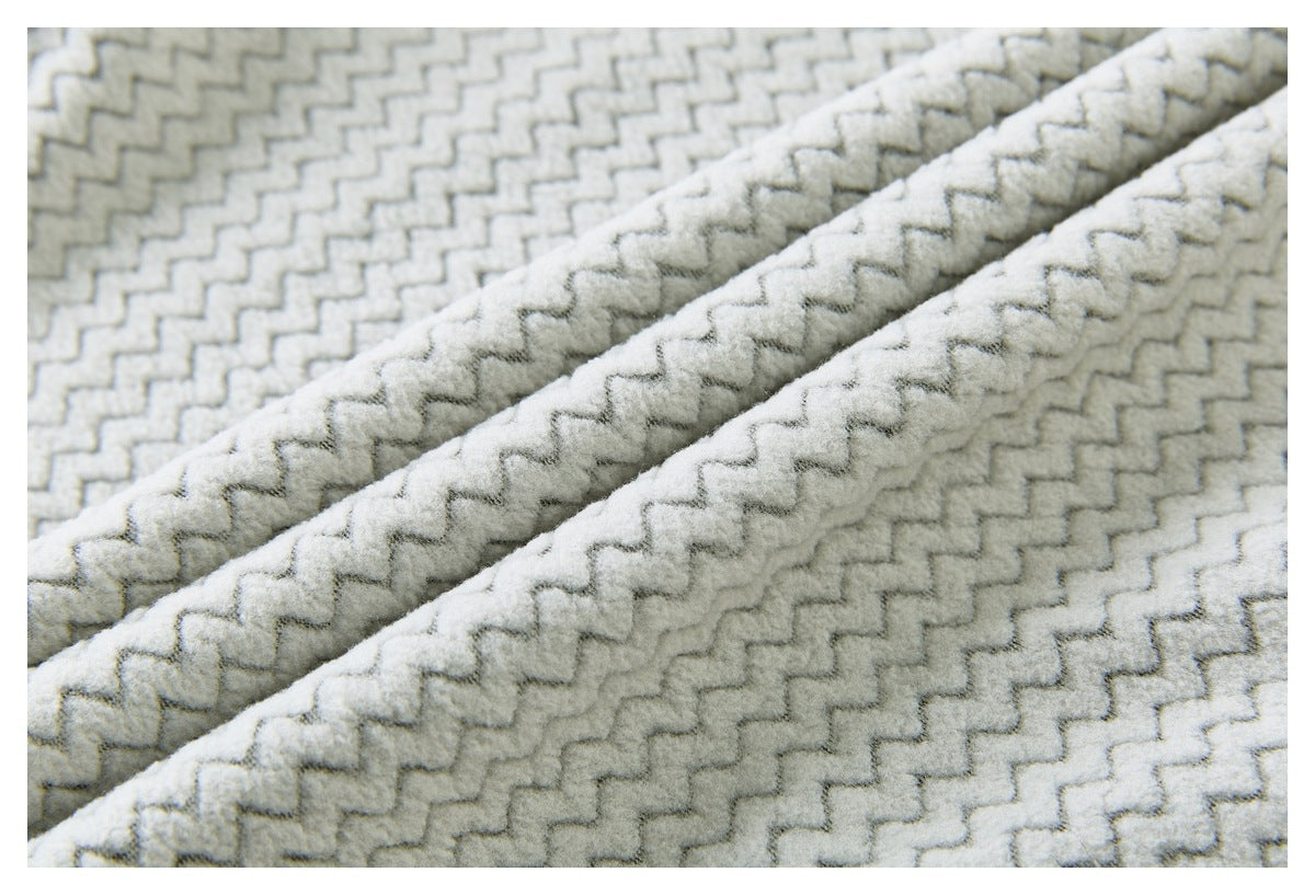 Macro view of raised zigzag texture on light gray fabric folded into soft diagonal ridges.