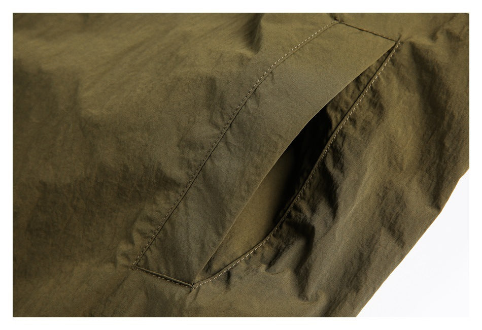 Close-up of an olive-brown garment pocket with a wide stitched flap and opening.