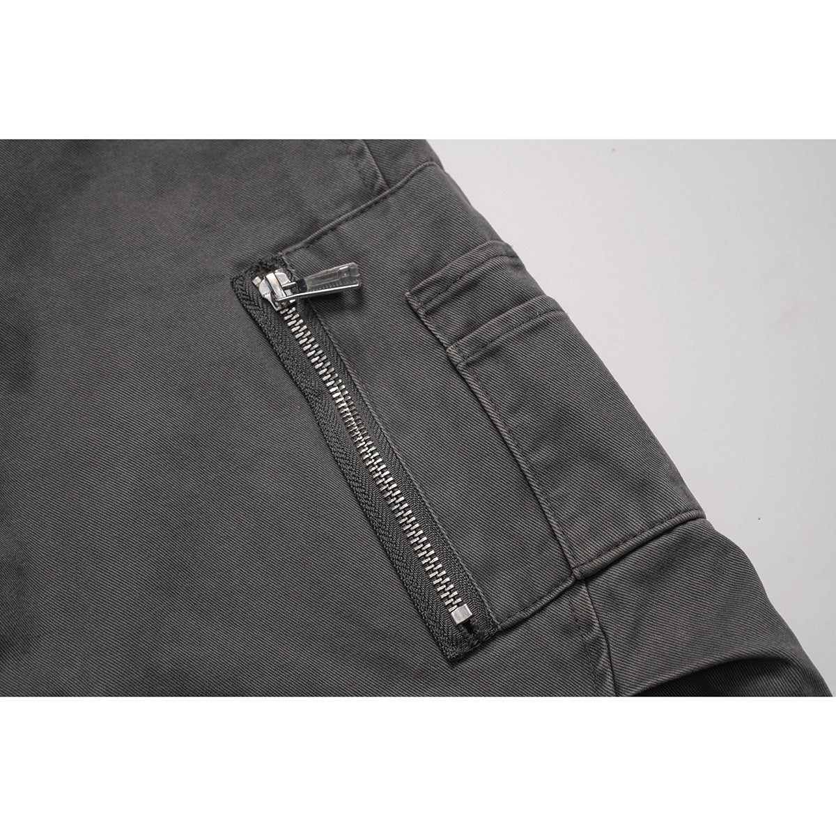 Close-up of a charcoal jacket sleeve utility pocket with a silver zipper.
