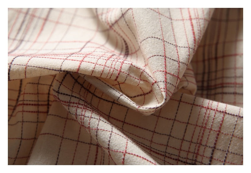 Close-up of folded cream plaid fabric, showing intersecting red and gray lines and a stitched edge.
