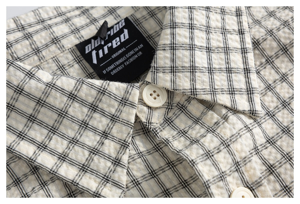 Close-up of an ivory plaid shirt collar, cream button, and black neck label.