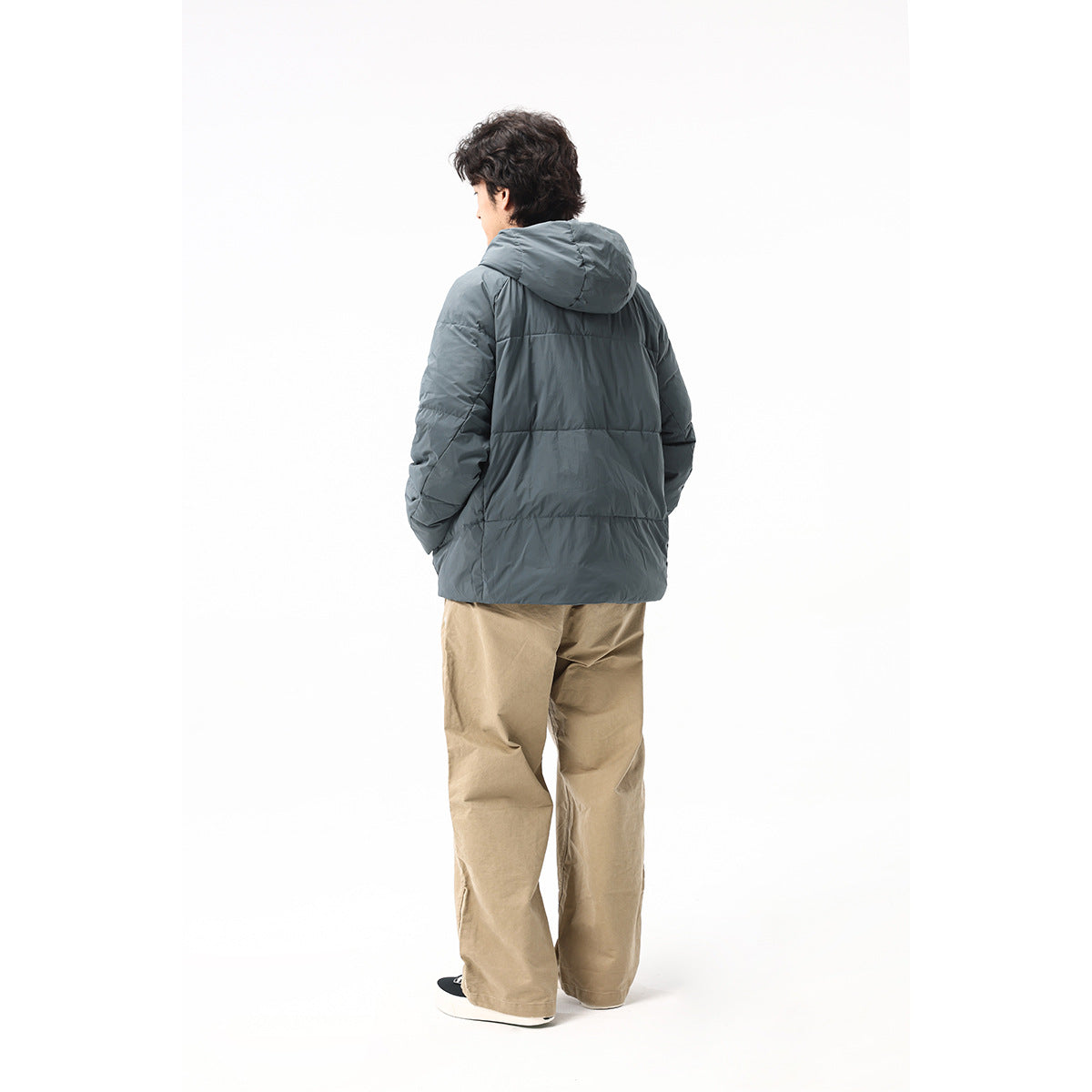 Rear view of a model wearing a slate-gray hooded puffer jacket with tan trousers.