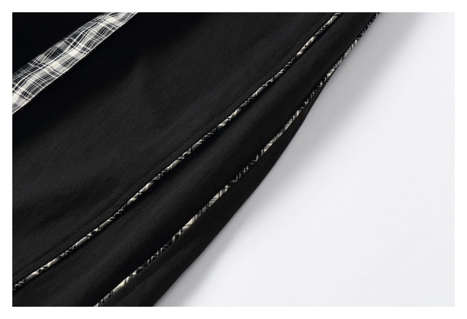 Close-up of black trouser fabric with narrow black-and-white plaid piping along the seams.