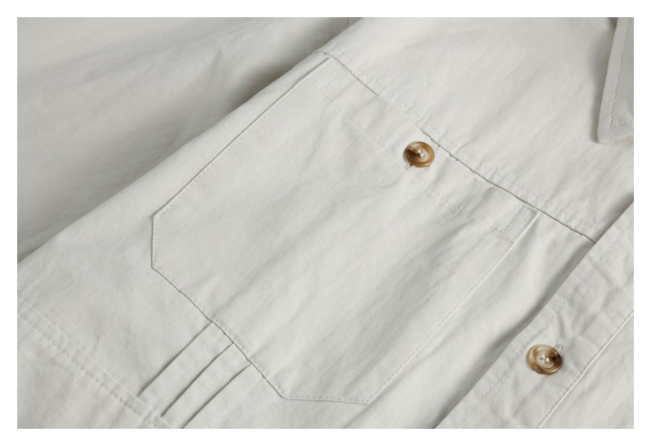 Close-up of an off-white shirt chest pocket with tan buttons and visible stitching.