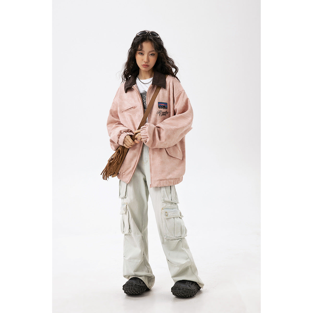 Model wearing a dusty pink zip jacket with a dark brown collar, chest embroidery, and roomy sleeves.
