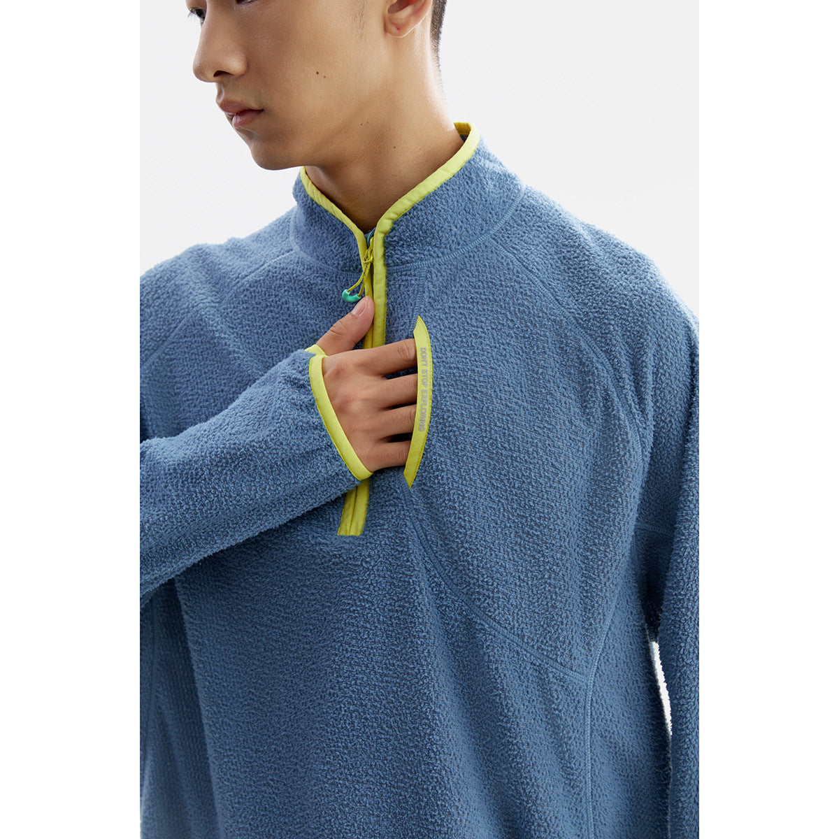 Close-up of a blue fleece pullover showing its yellow-trimmed collar, front opening and chest pocket detail.