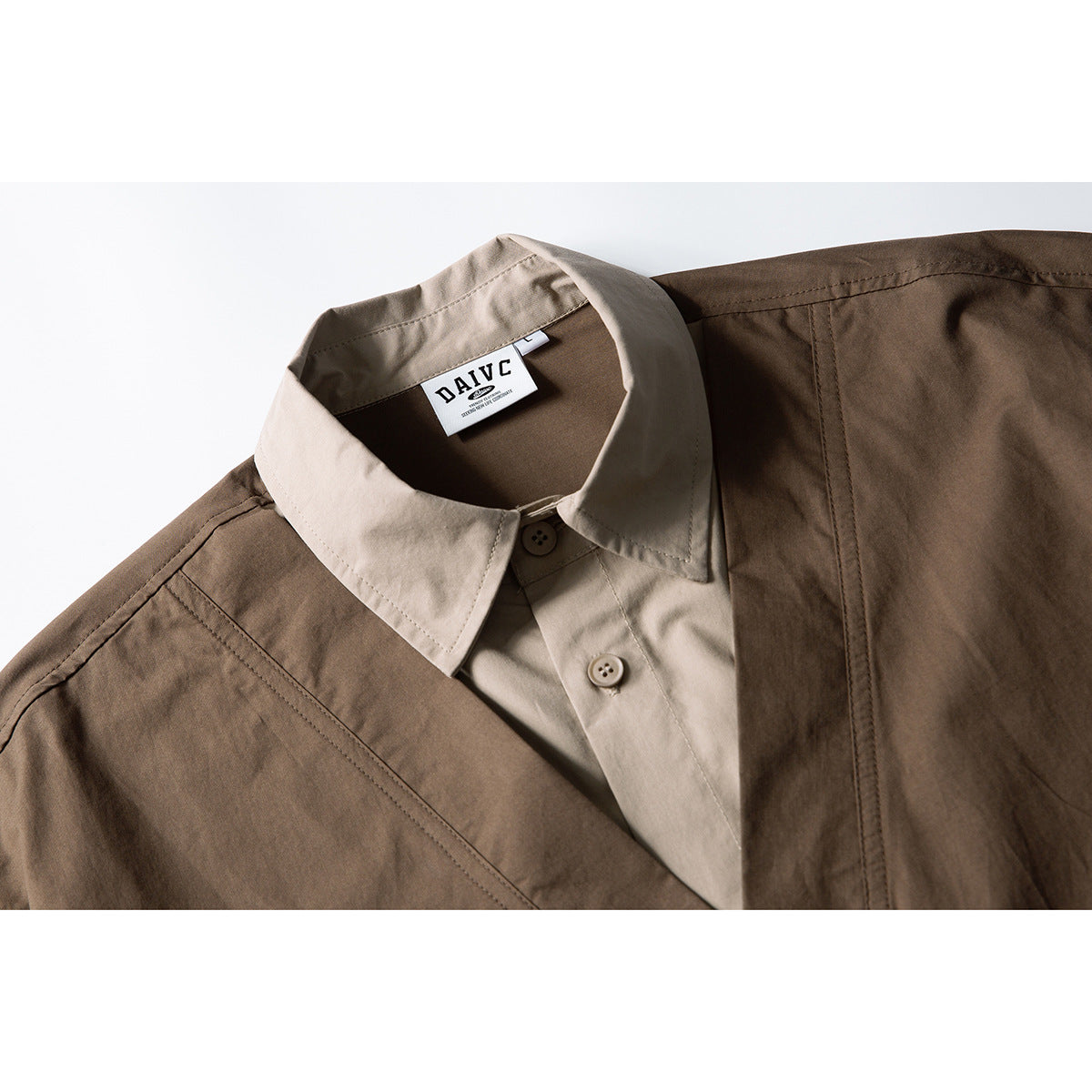 Close-up of a brown utility vest layered over a beige shirt, showing the collar, buttons and neck label.