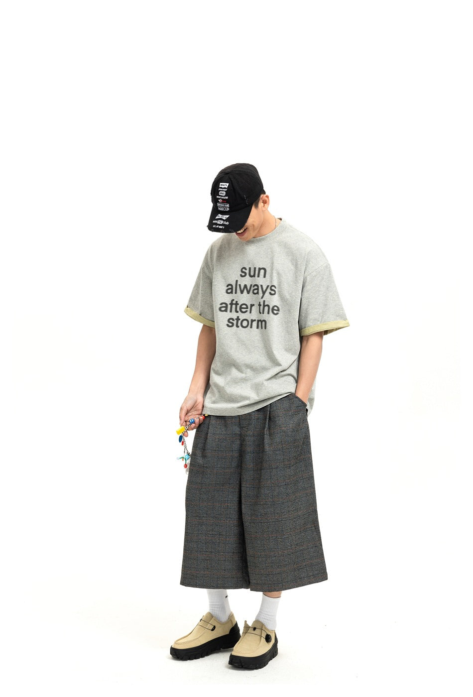 Model looking down wearing gray 'sun always after the storm' T-shirt with plaid wide-leg shorts and beige shoes