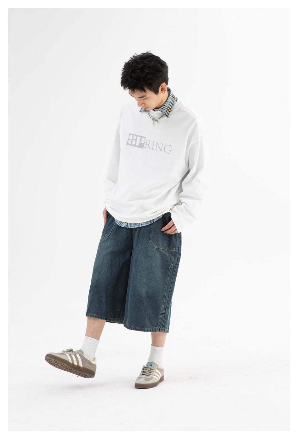 Model wearing a white SPRING graphic long-sleeve shirt with a blue plaid collar and wide dark denim shorts.