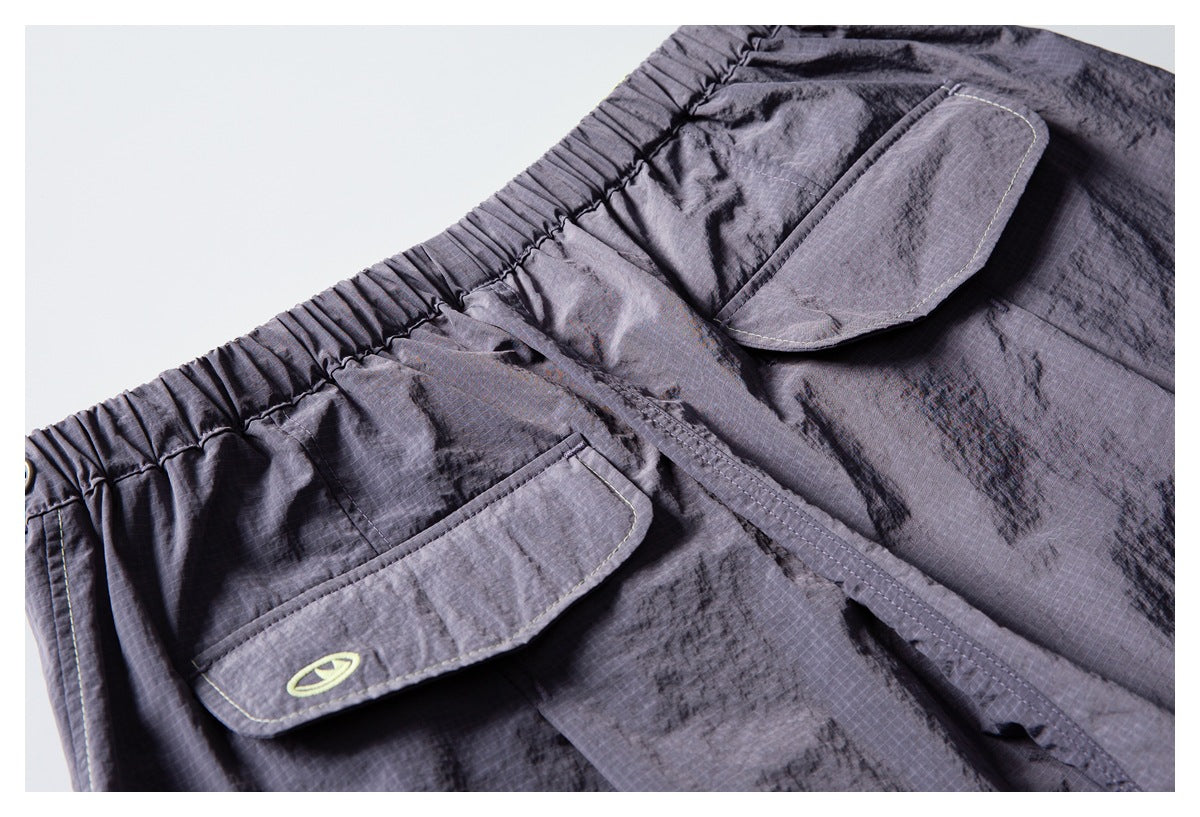 Close-up of charcoal-gray pants with two flap pockets, pale contrast stitching, and a small lime emblem.