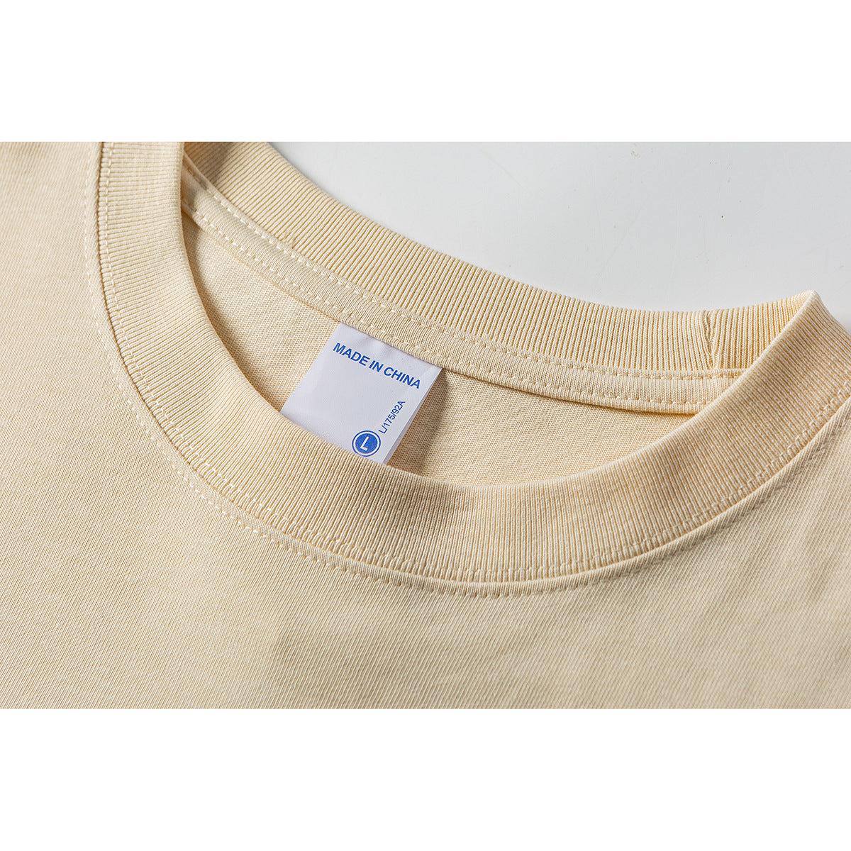Close-up of a cream T-shirt's ribbed crew neck and inner label marked “Made in China.”