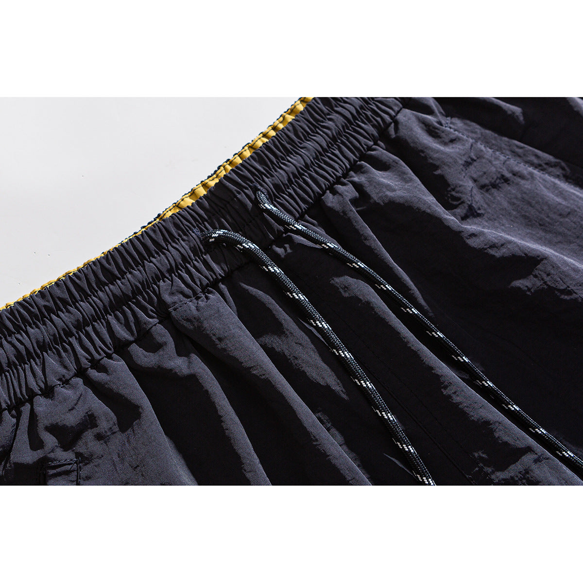 Close-up of black shorts showing a gathered elastic waistband, black drawstrings and a glimpse of yellow lining.