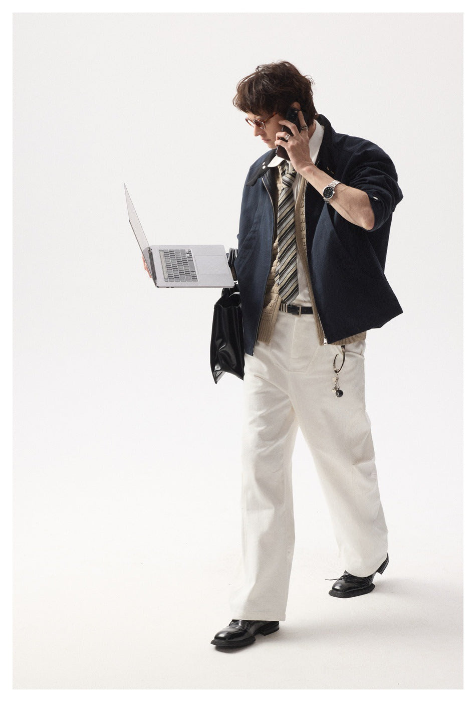 Full-length model wearing a navy zip jacket over a beige knit layer, white shirt, striped tie and white trousers.