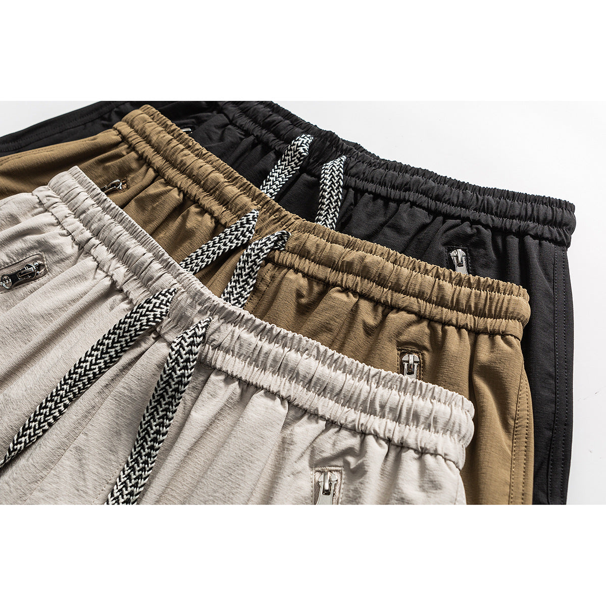 Close-up of black, brown, and light beige cargo shorts showing elastic waistbands, braided drawstrings, and zip pockets.