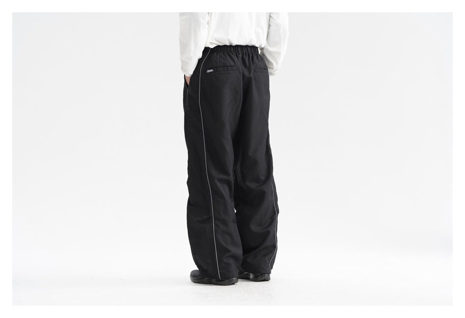 Rear view of a model wearing black loose-fit pants with an elastic waist, back pocket, and side piping.