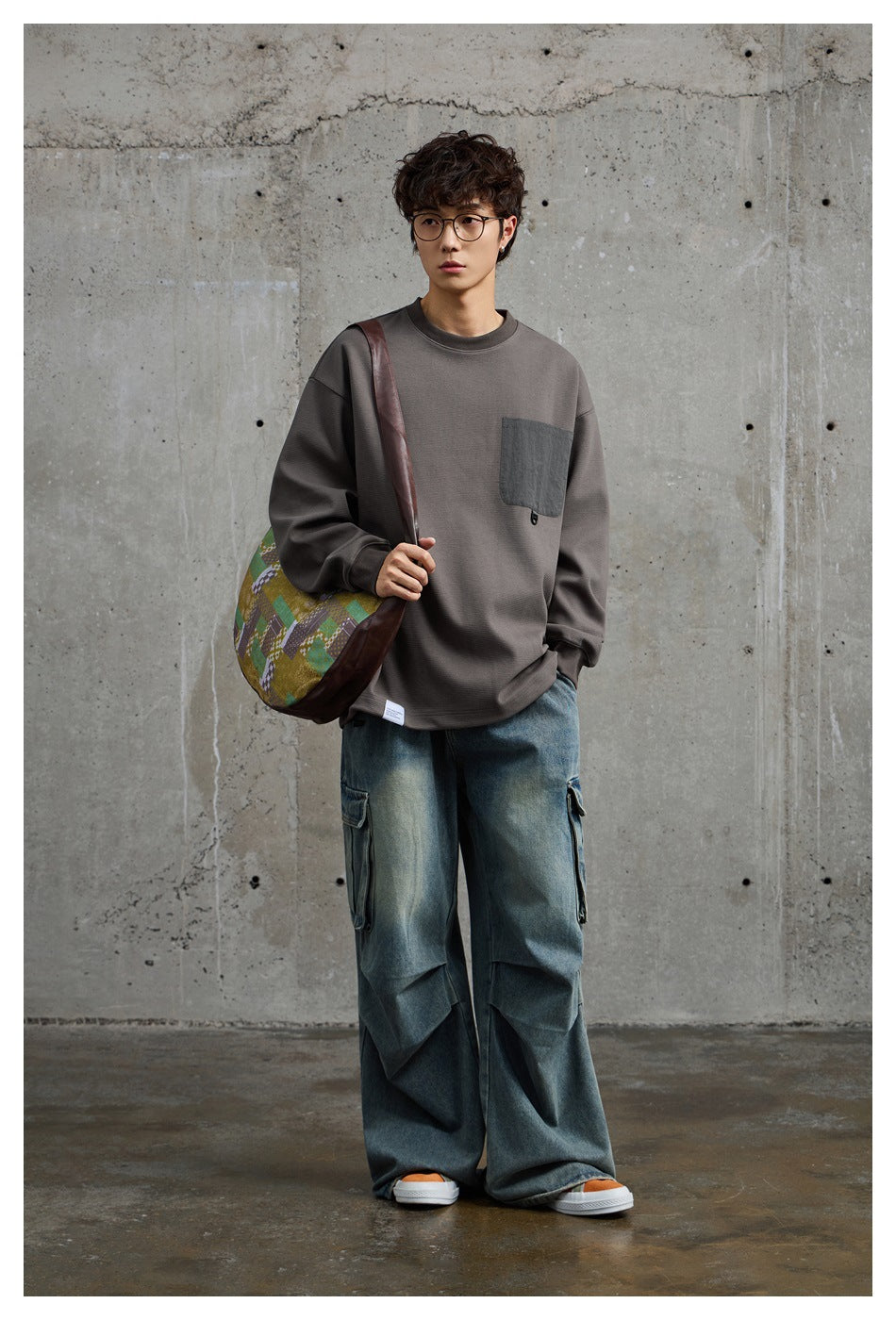 Full-length view of a model in a charcoal gray pocket sweatshirt and loose blue cargo jeans.