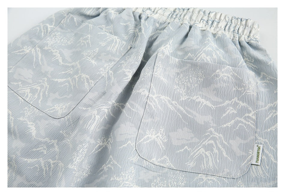 Close-up of the back of pale blue shorts with an elastic waistband, two patch pockets, and a mountain print.