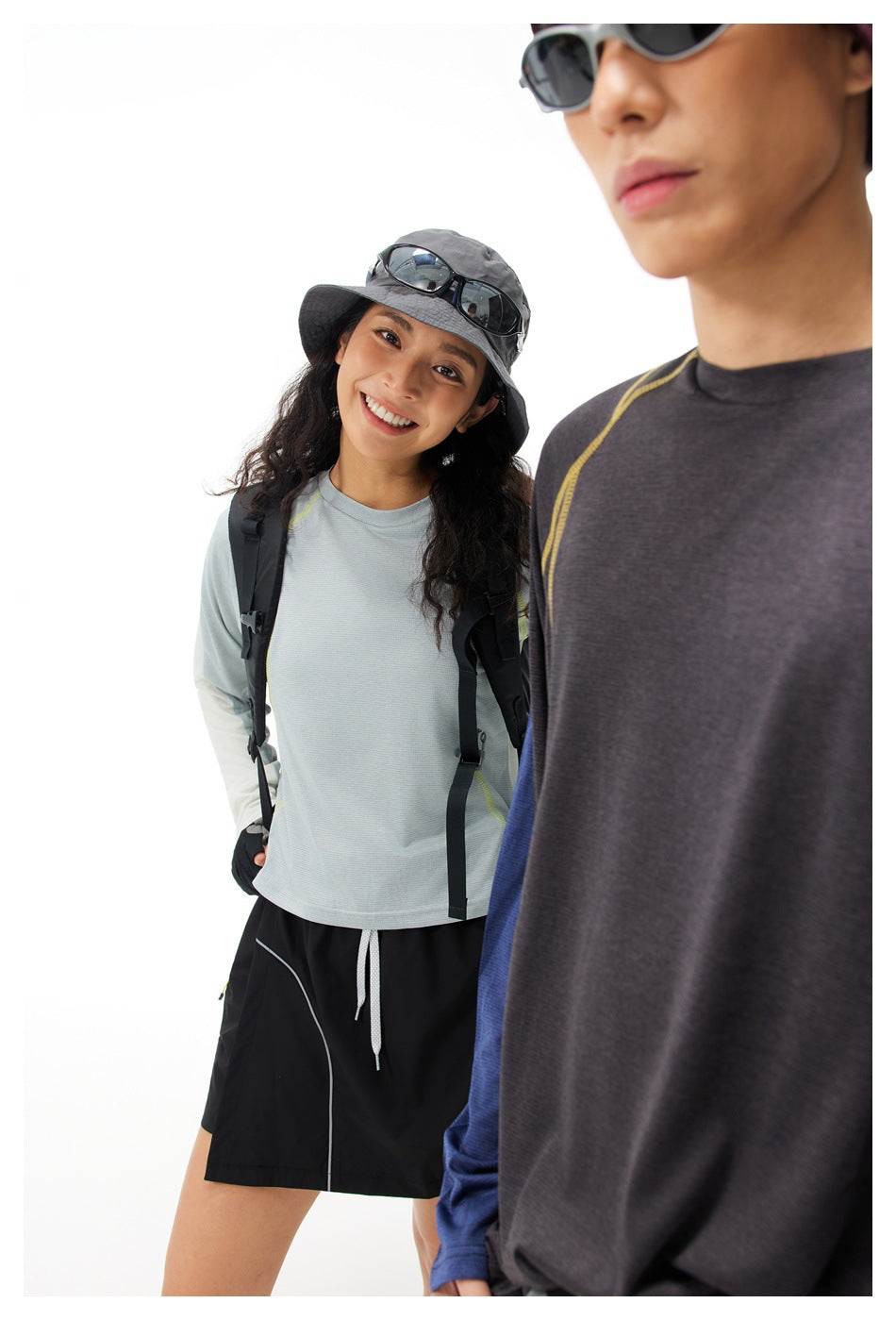 A woman wearing a pale blue long-sleeve top and black skirt stands behind a partially cropped model in a charcoal top.