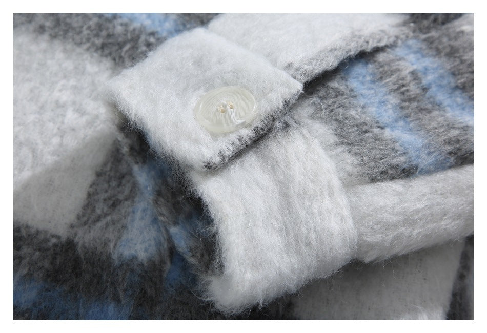 Close-up of a white button on the cuff of a fuzzy blue, gray, and white plaid garment.