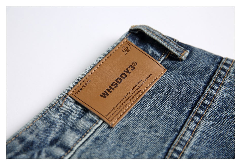 Close-up of a brown leather WHSDDY3 label sewn onto the waistband of blue jeans.