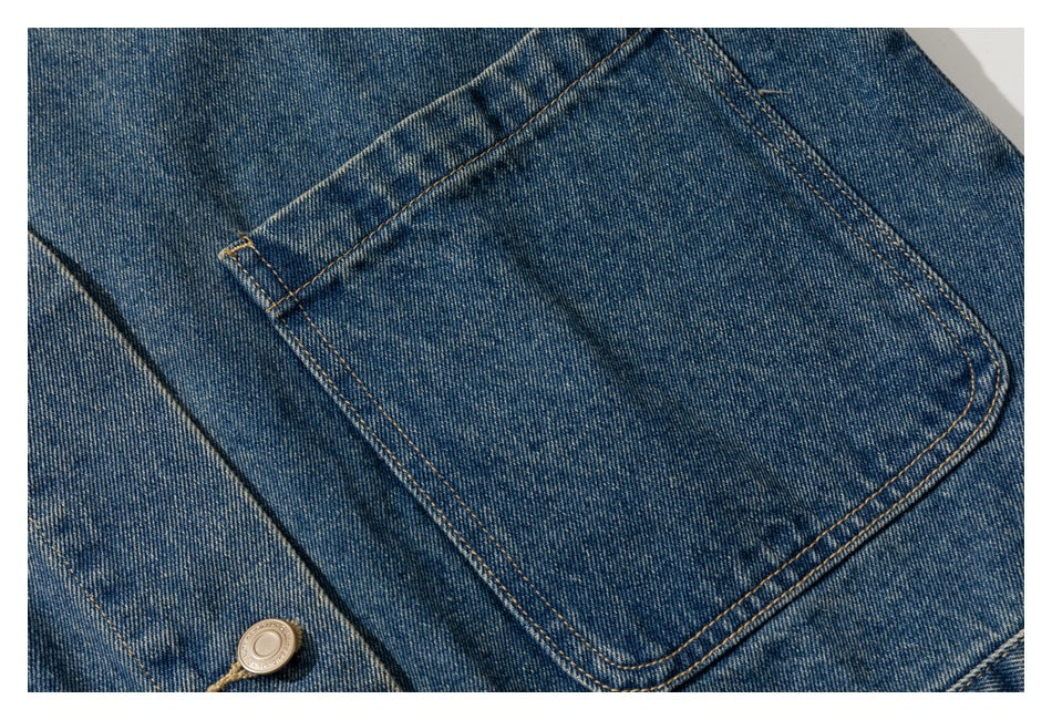 Close-up of a blue denim jacket pocket with tan stitching and a metal button.