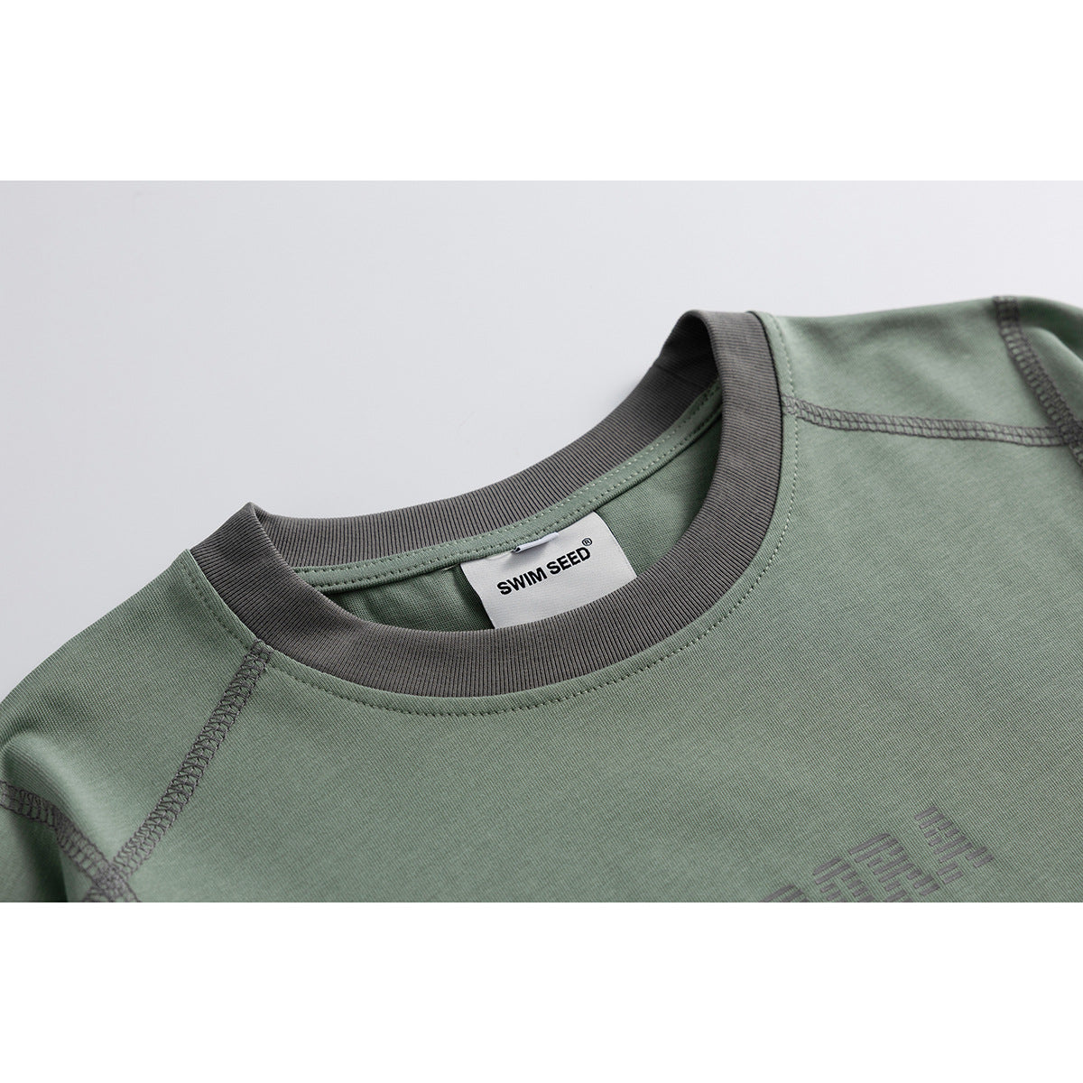 Close-up of a sage green T-shirt with a charcoal ribbed crew neck, contrast stitching and a visible neck label.