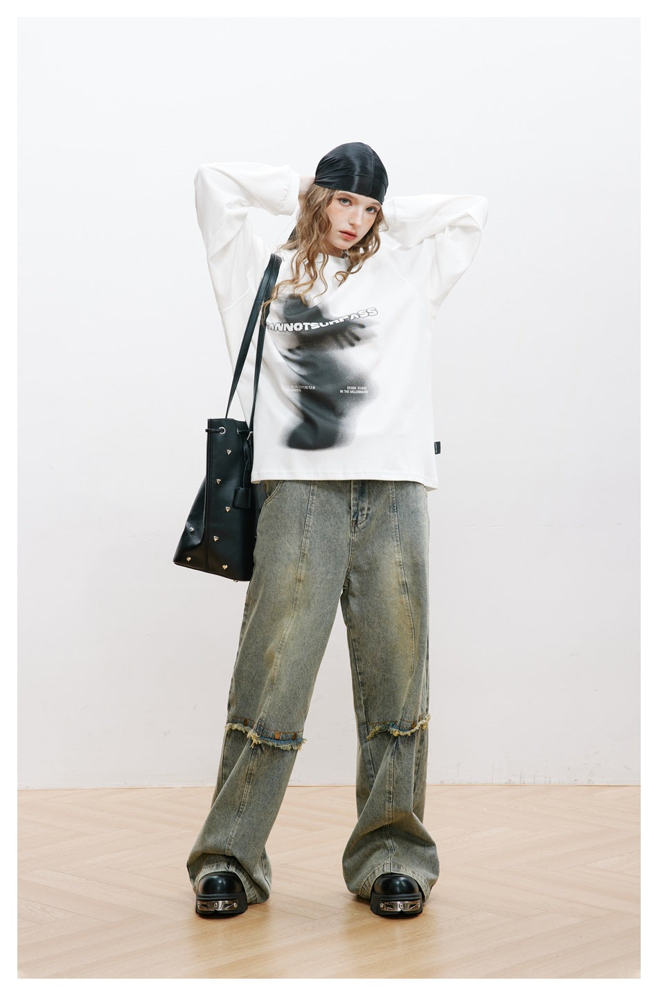 Model wearing a white oversized long-sleeve top with a black graphic and faded wide-leg jeans.