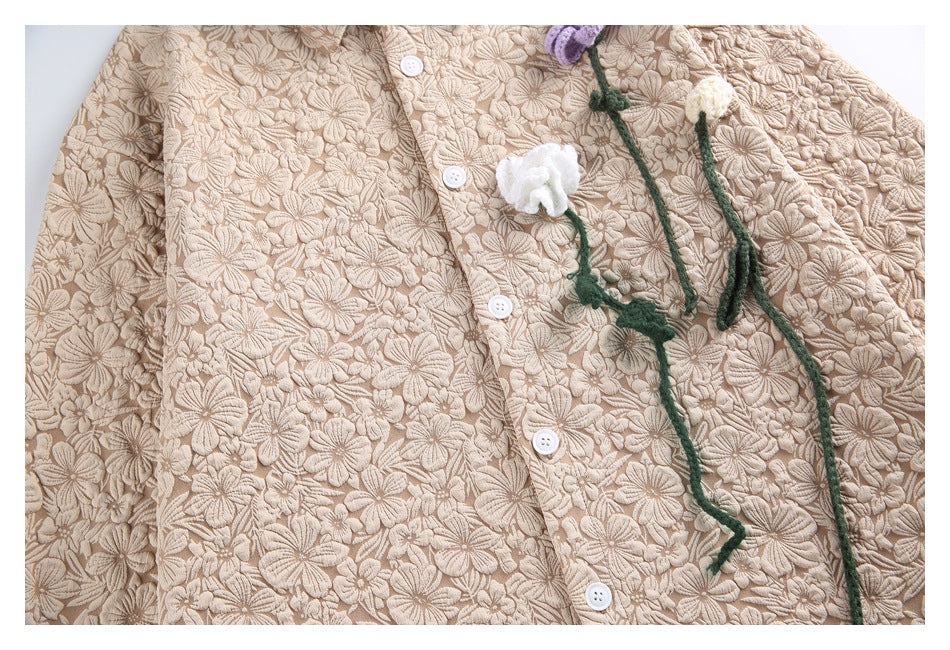 Close-up of a beige floral-textured button-front garment with white buttons and dangling green stems topped with yarn