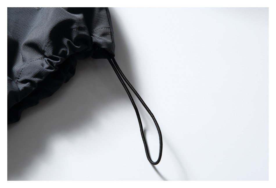 Close-up of the jacket’s gathered charcoal hem and hanging black adjustment cord.