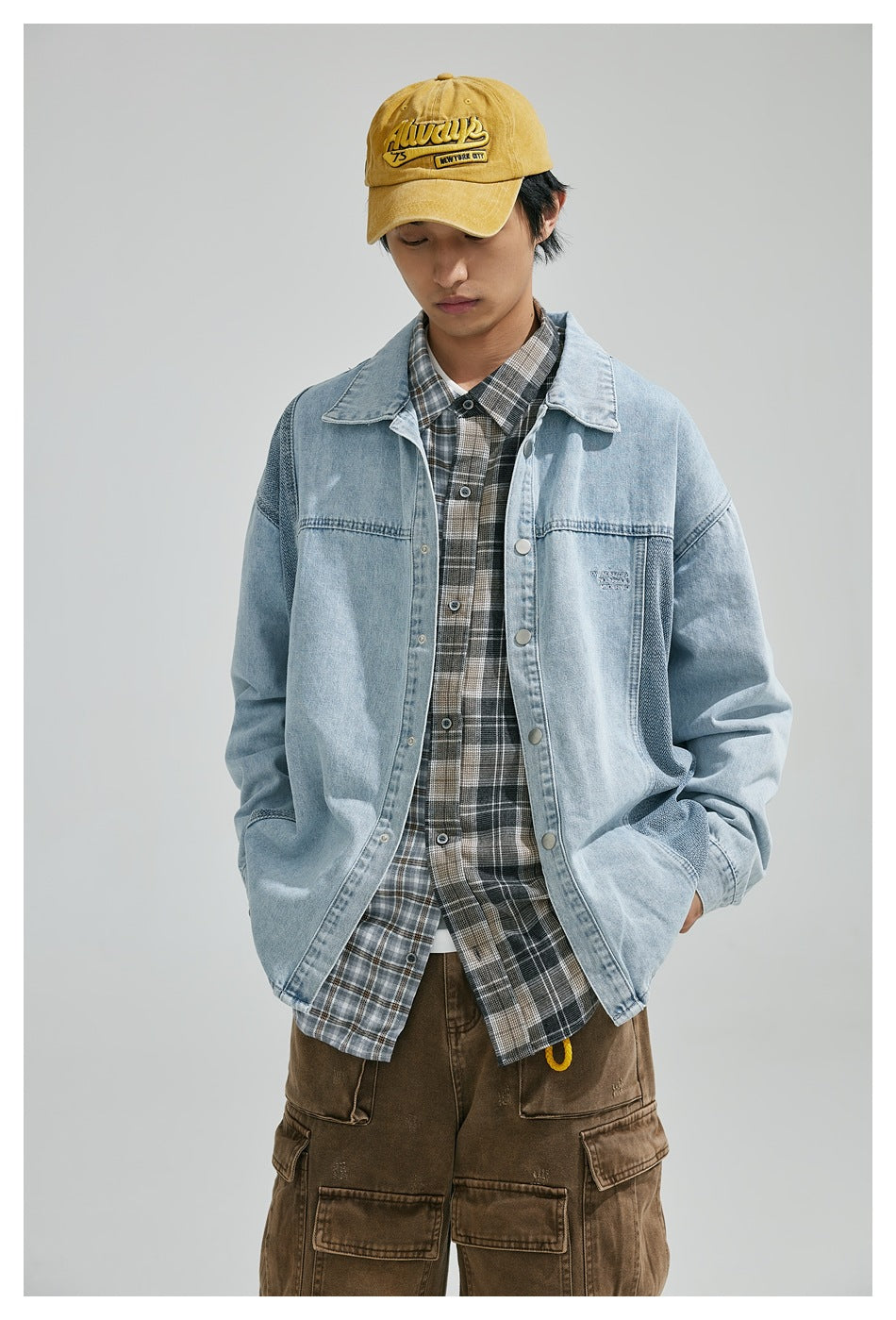 Front view of a model wearing a light blue color-block denim shirt jacket over a plaid shirt.